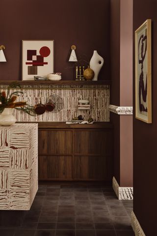 An earthy kitchen with brown walls, a white and brown backsplash and island, and dark square floor tiles