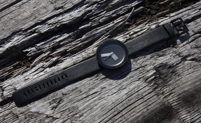 A minimalist black watch lying on top of a rough piece of wood