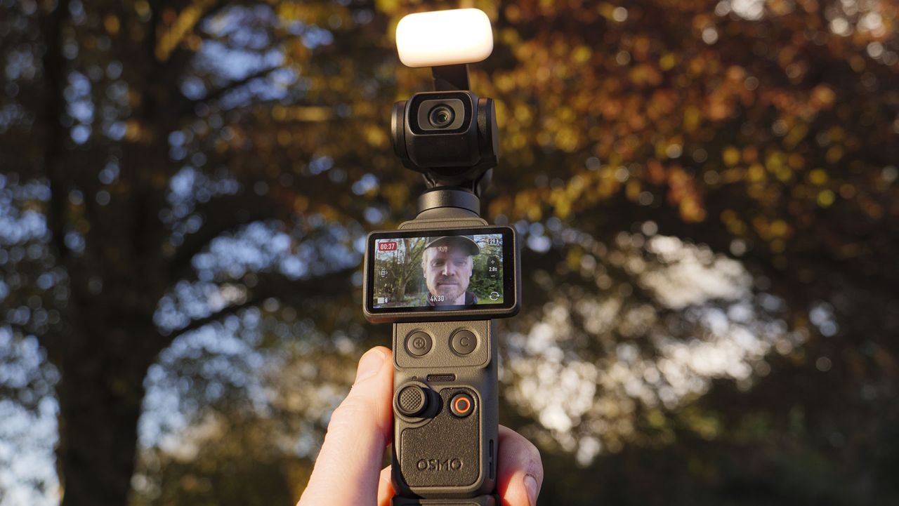 DJI Osmo Pocket 4 vlogging camera with natural background at golden hour, and the user in the frame of the screen