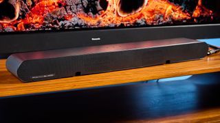 the samsung hw-s60D soundbar photographed on a wooden coffee table with a panasonic tv and a samsung soundbar against a blue background