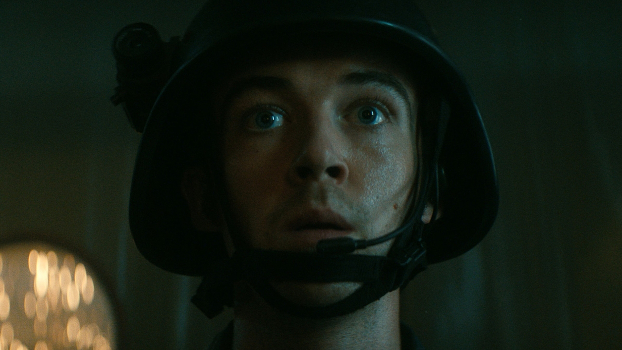 Still from the TV show Alien: Earth. Close up of a dazed soldier. They are wearing a helmet with a small camera attach to the side.