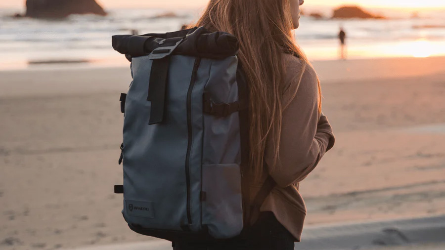 A person wearing the Wandrd Prvke camera backpack on a beach