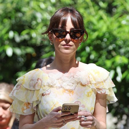 Dakota Johnson walking in New York City wearing a floral midi Doên dress, Nike sneakers, and cat-eye sunglasses.