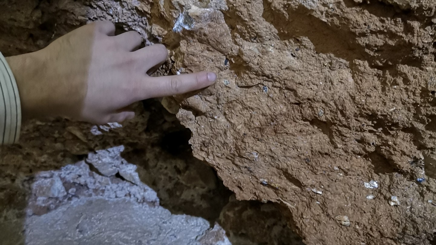 A close up of a hand pointing to evidence of human artifacts embedded in a brown rock of a cave.