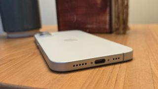 Apple iPhone 16 smartphone face down on wooden table showing USB-C port and speakers