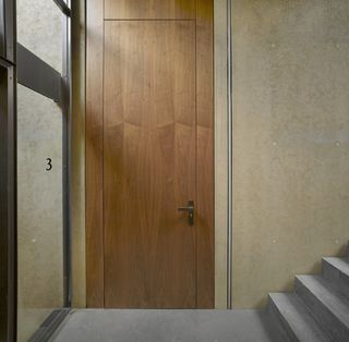 Sandy-coloured interior walls complemented by warm timber doors with a floor to ceiling glass window on the left. and grey staircase on the right