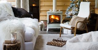 Cozy cabin room with white sofa and fluffy beanbag in front of a cozy log burner with a game of chess on the floor