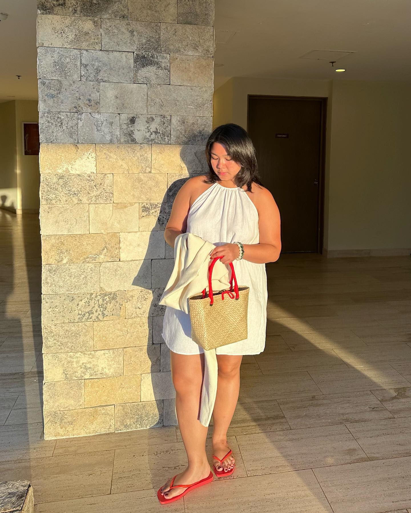 Influencer Mariana wears a white baby doll dress wears red flip flops and a red handled whicker bag