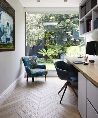 Study area with parquet floor, desk and blue armchair in front of large picture window to garden.