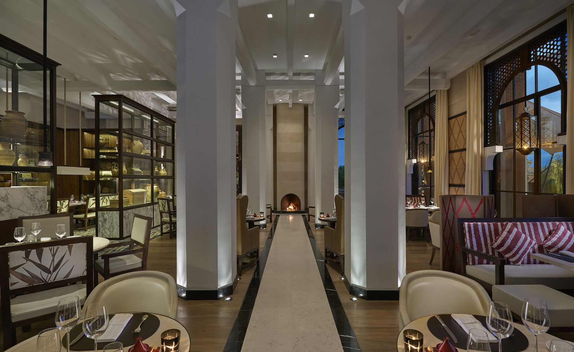 A hotel dining area with round decorated tables, tile and wooden floors, large pillars and large glass windows.