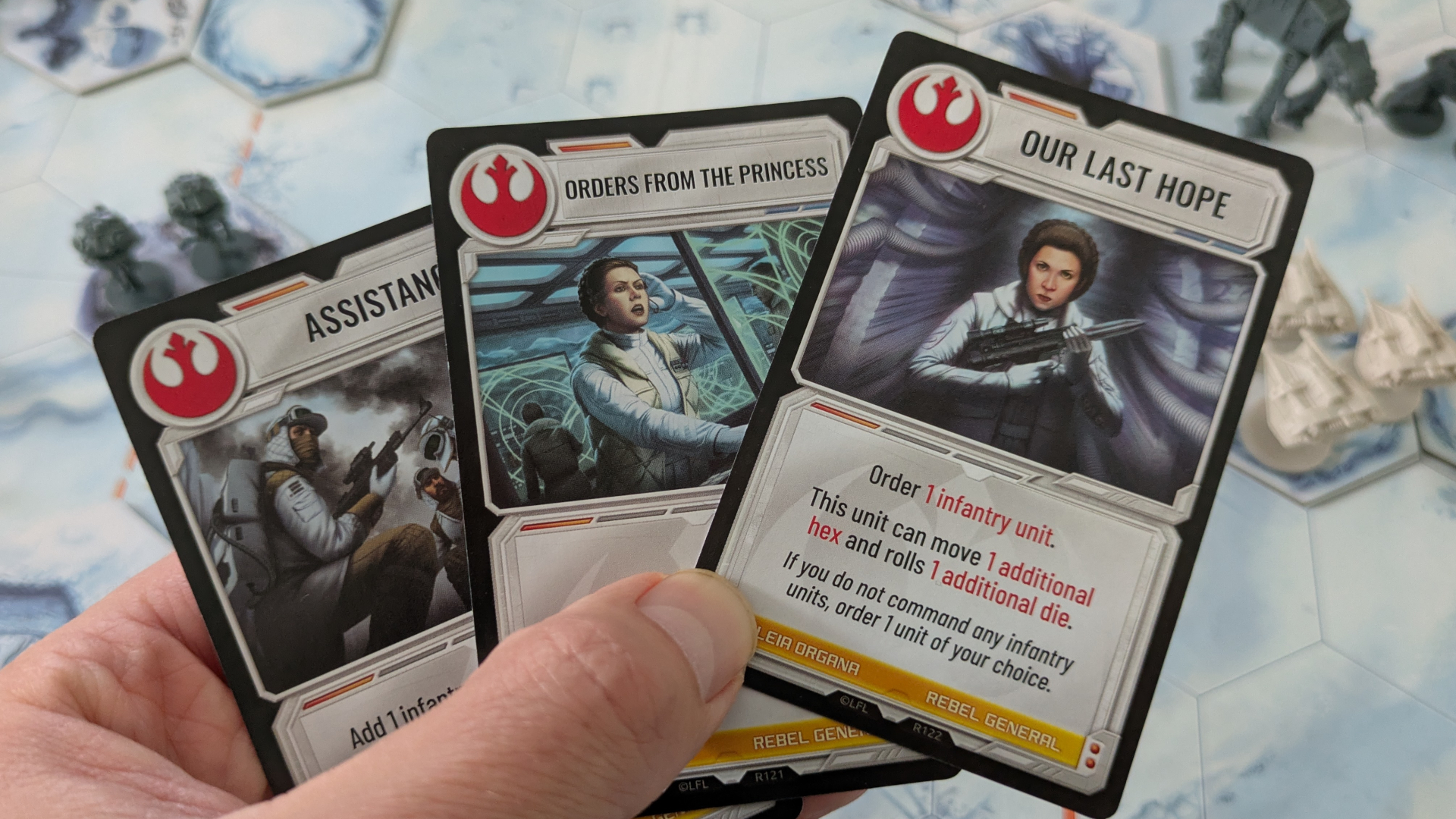 A hand holds cards from Star Wars: Battle of Hoth in front of a board full of miniatures