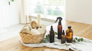 natural cleaning products in generic black containers, and accessories in a basket, sat in front of a window