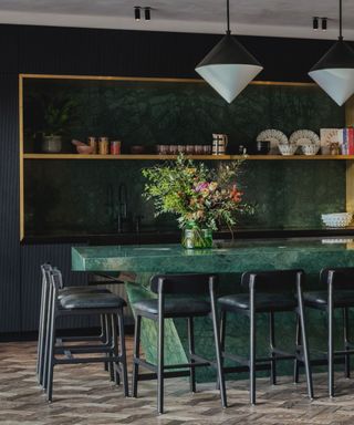 dark green kitchen with marble island and black chairs