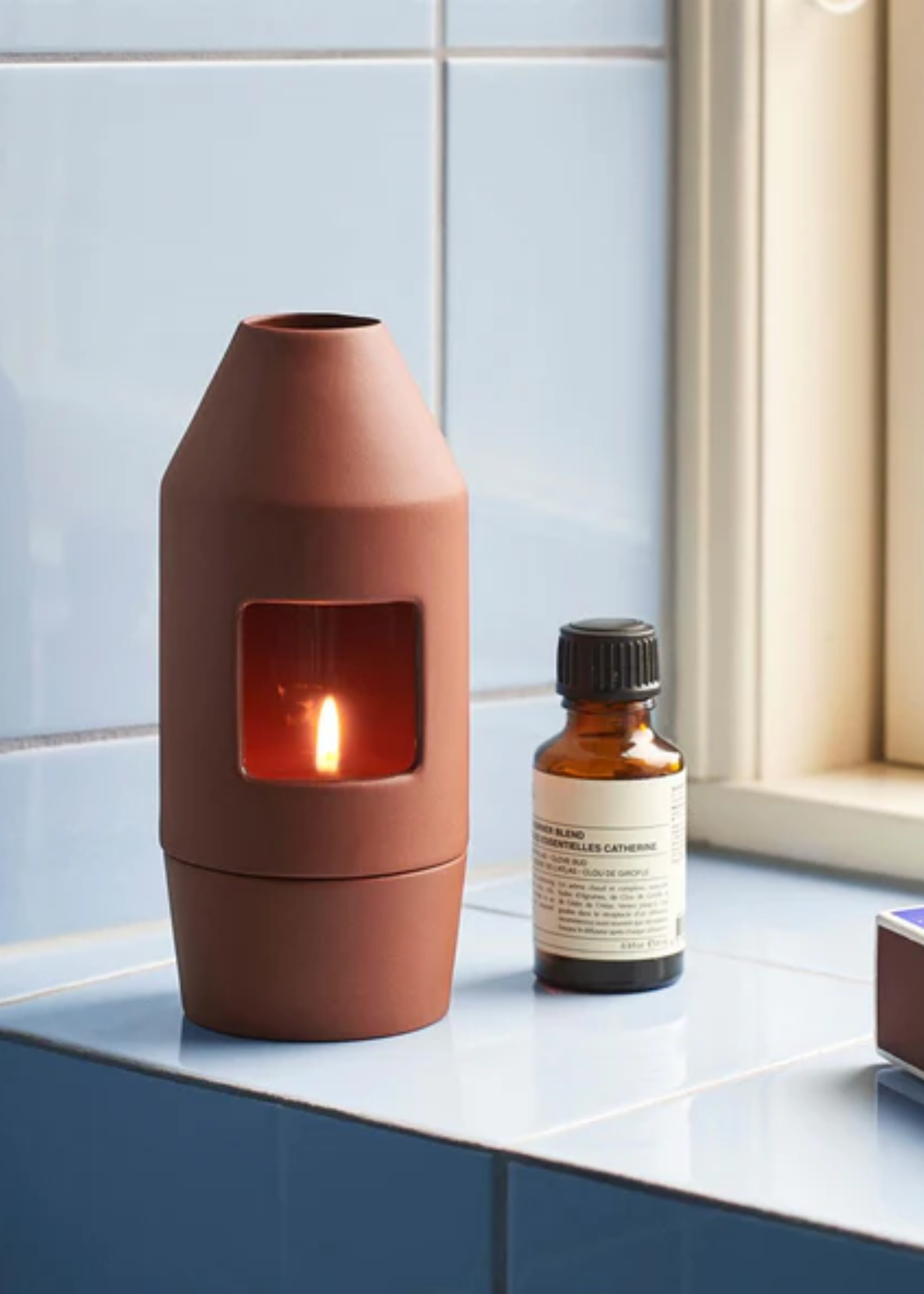 A brown oil burner beside an amber bottle of essential oils on a blue tiled ledge
