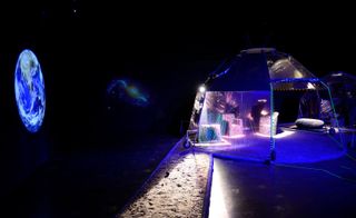 Futuristic image, moon terrain, open tent on wheels, lights on inside, stone seating, black background, projection of the earth and a galaxy in the distance on the left