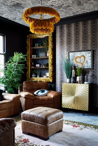 A dark living room paint color idea with snake skin wallpaper, feathered pendant, Art Deco starburst cabinet and brown leather sofa