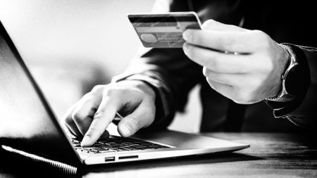 Detail of a person holding a credit card next to a laptop computer