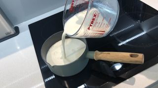 Milk being added to a saucepan on a stove