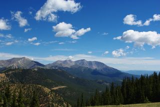 Clouds hover over the Rocky mountains, as seen from a distance.