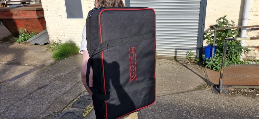 A man carries a Voodoo Lab Dingbat Medium pedalboard in its carry case