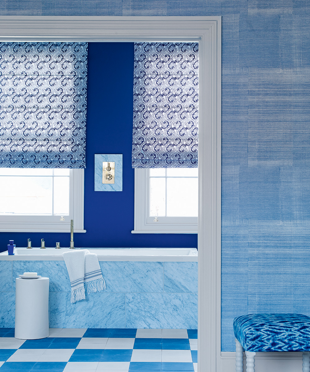 A blue bathroom with a blue upholstered stool and blue and white checkered flooring