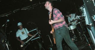 H&uuml;sker D&uuml; play live in the mid '80s, with Bob Mould playing a Flying V and wearing a pink and gray plaid shirt.