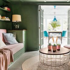 Cosy snug living room with green walls and pink chairs with double doors leading to conservatory