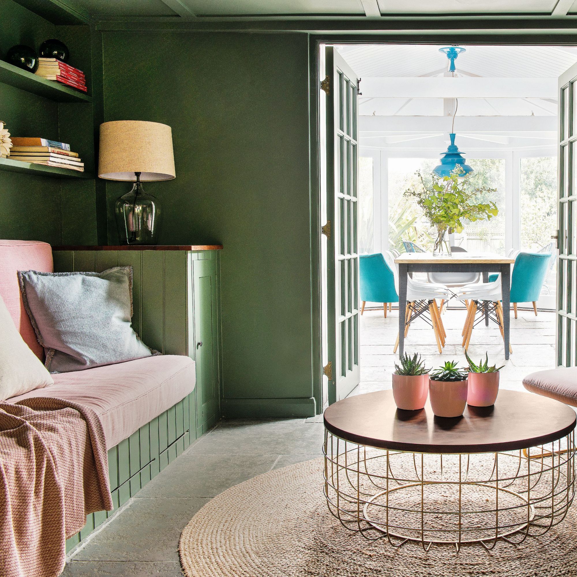 Cosy snug living room with green walls and pink chairs with double doors leading to conservatory