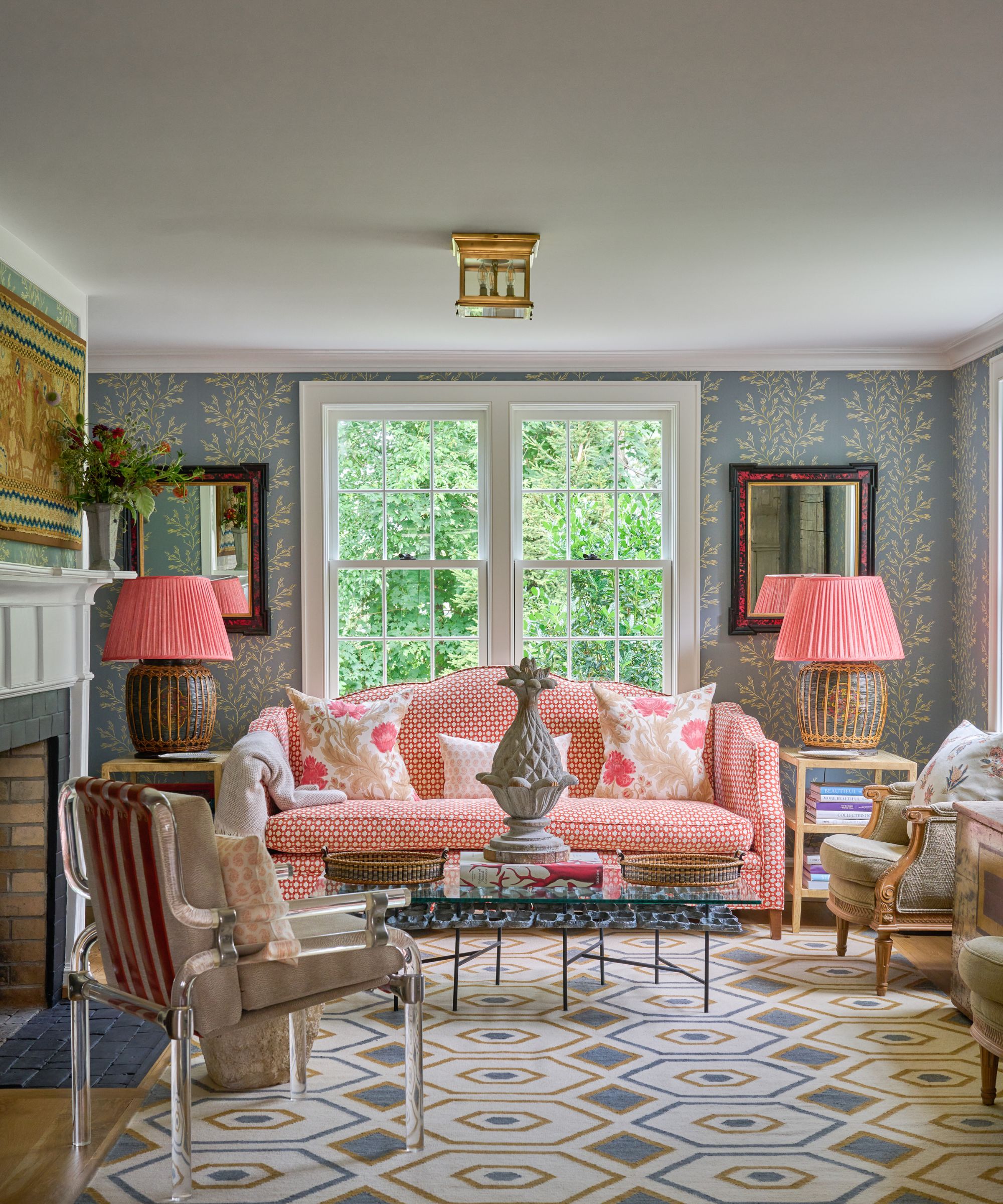 Living room with blue wallpaper and vintage furniture, a pink and white patterned sofa, wooden accent chairs and a patterned rug