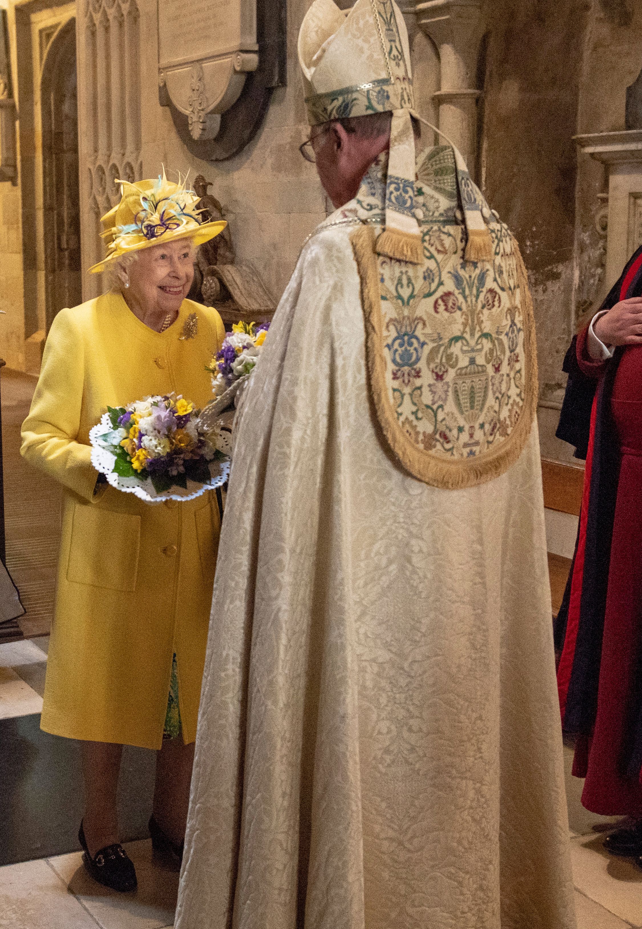 Queen Elizabeth in a yellow coat and hat talking to a bishop