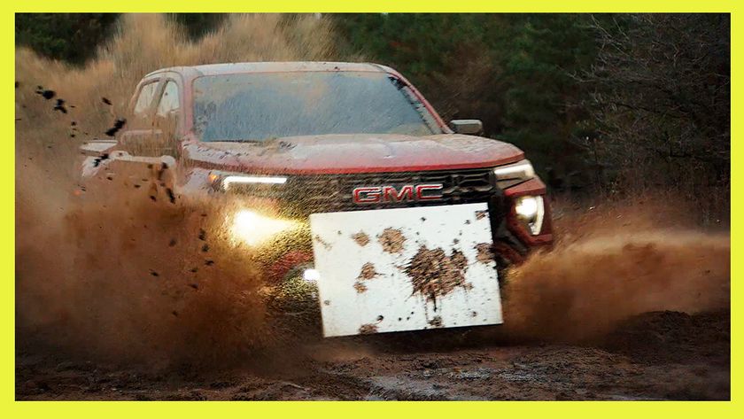 A GMC truck drives through mud with an art canvas attached to its front grille