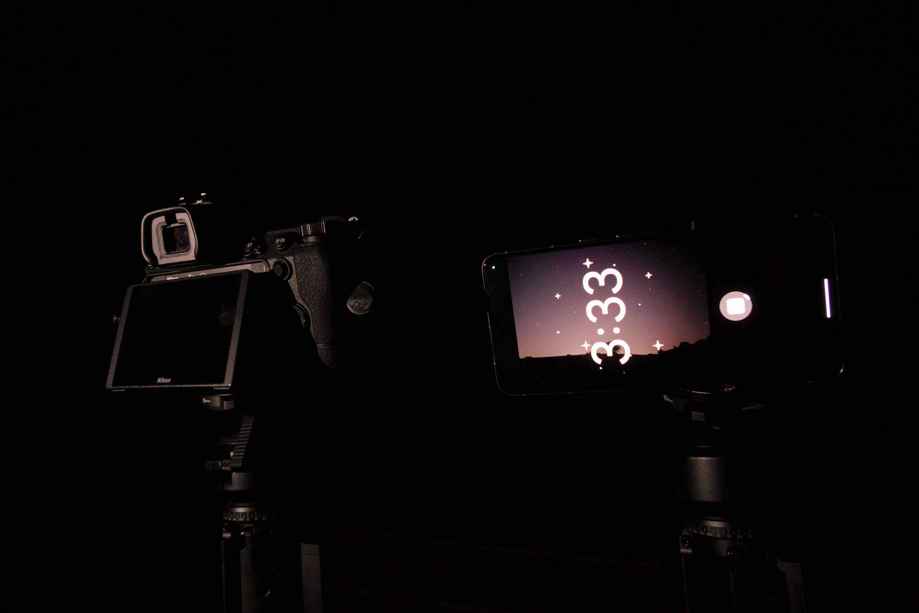 Pixel phone and Nikon mirrorless camera side by side mounted to tripods at night, with the astrophotography mode active on the Pixel