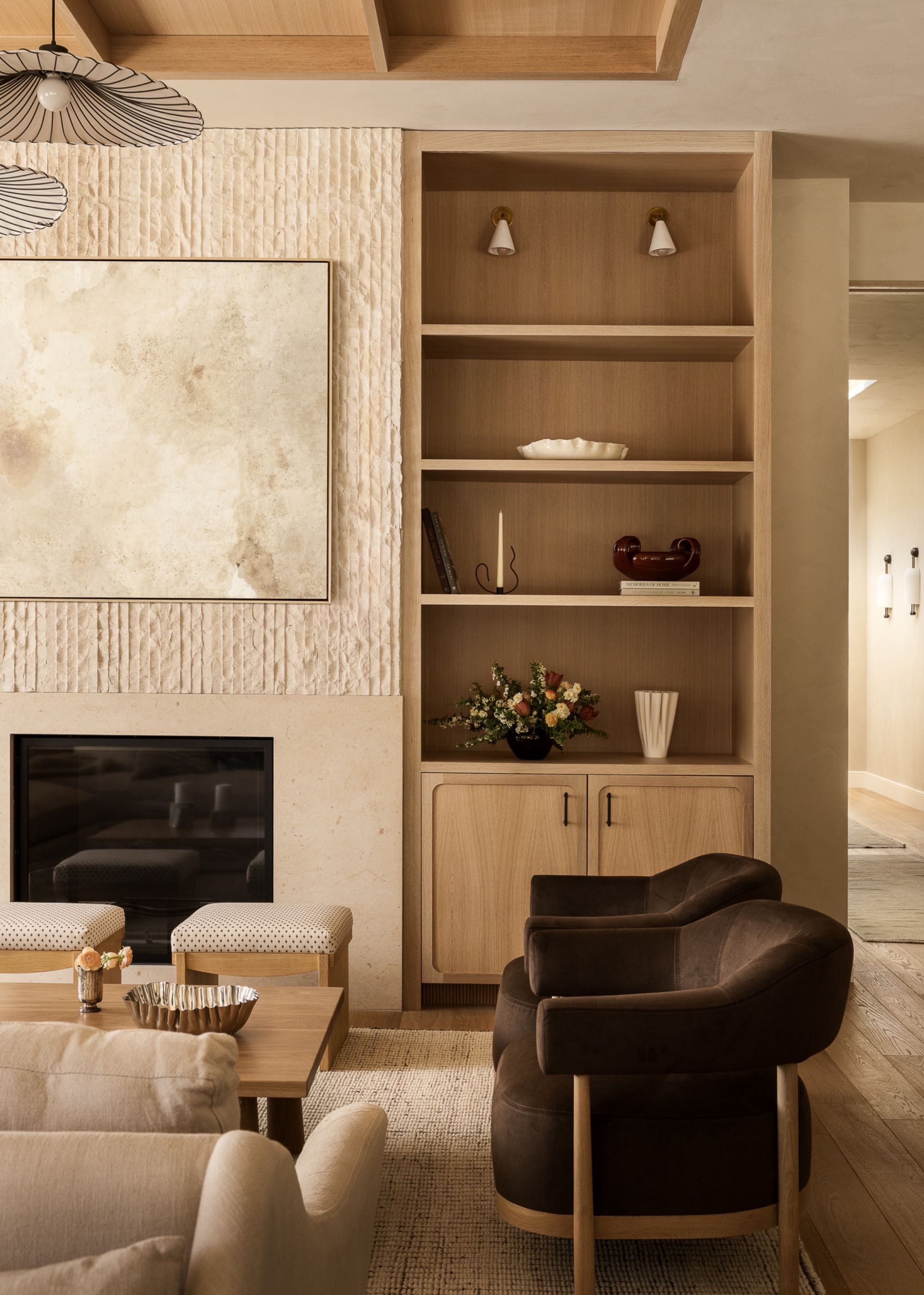 A modern neutral living room with a built-in fireplace with a textured wall and wooden storage and shelving next to it behind two dark brown modern armchairs