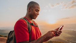 Man wearing a backpack holding his phone in the outback