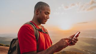 Man wearing a backpack holding his phone in the outback