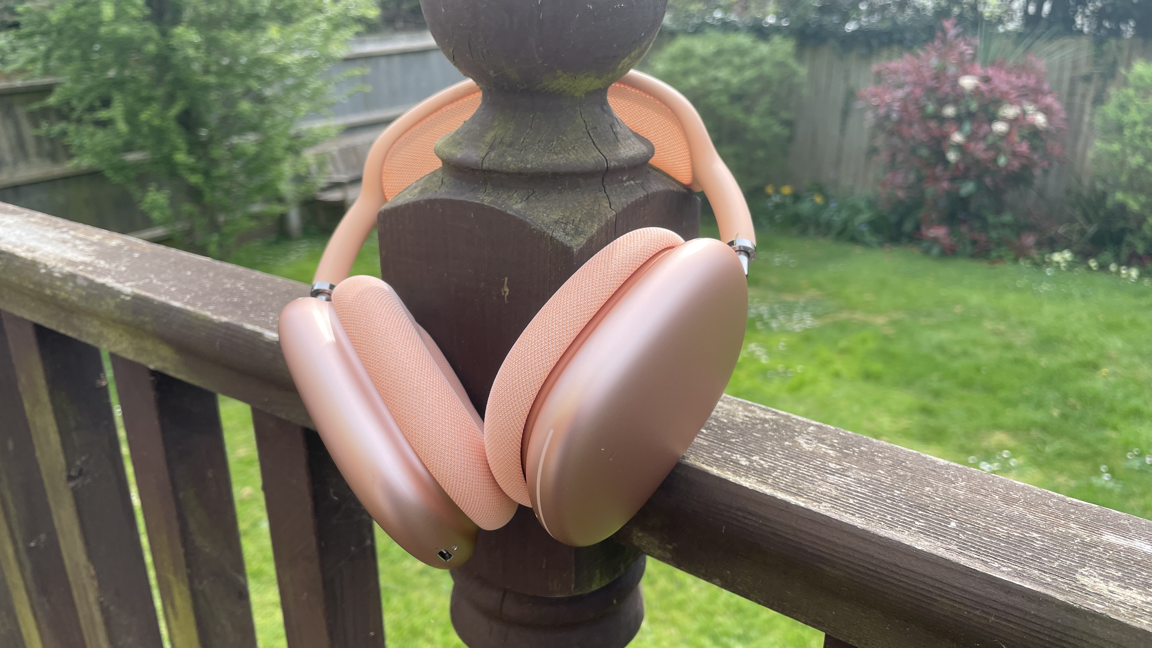Apple AirPods Max 2 in orange with AirPods Max just visible in purple, outside in a garden on a bench, held in a hand