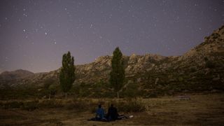 two people sit on a blanket in a field under the stars