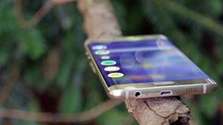 En Galaxy S6 Edge ligger på en gren utomhus med skärmen aktiv.