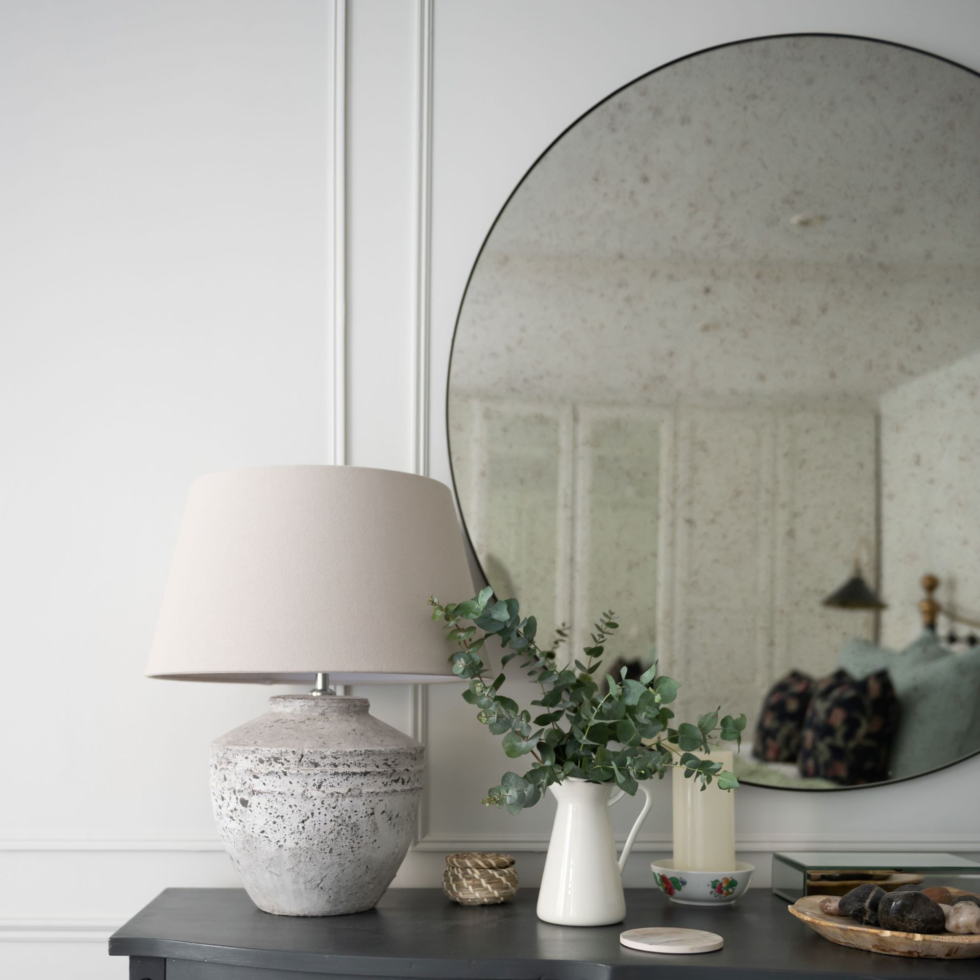 Dark wood dresser in bedroom with lamp and decor displayed on top with round circle mirror on wall