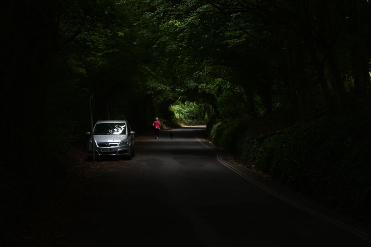 A person running down a road under tree cover