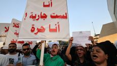 A group of Iraqi men and women protests a proposed law, holding signs and yelling