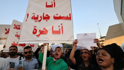 A group of Iraqi men and women protests a proposed law, holding signs and yelling