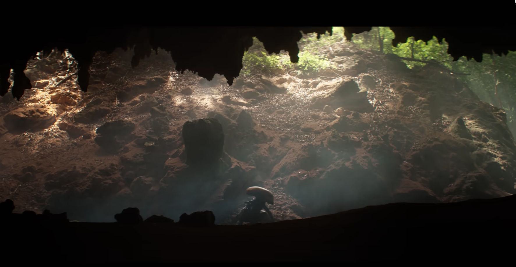 an alien crouching at the mouth of a forest cave