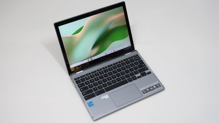 An open and powered on silver laptop with a black keyboard against a white background, showing a curvy green image on its screen.