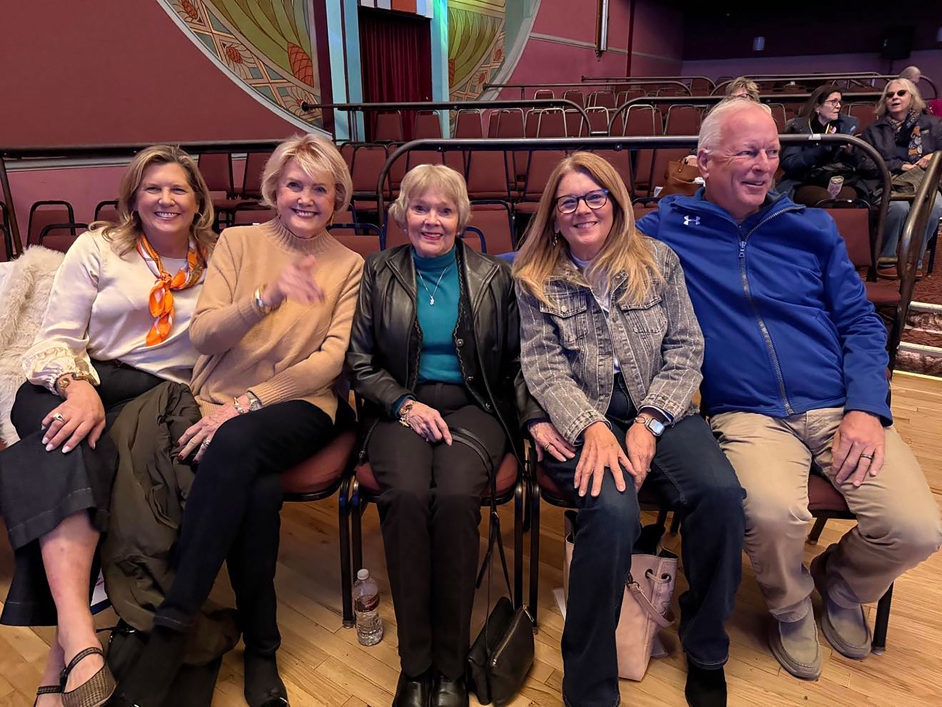 four women and a man sit inside a movie theater and pose for a photo together