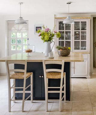 White kitchen with wooden island and chairs with hanging lights above next to cupboards