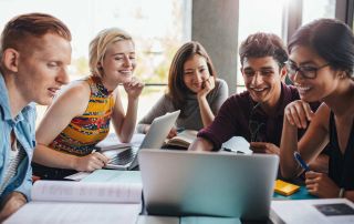 Five teens studying and laughing with laptop computers