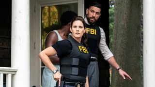 Special Agent Maggie Bell and Special Agent Omar Adom "OA" Zidan wearing bulletproof FBI vests while standing outside a house. Maggie is holding a gun in her holster.