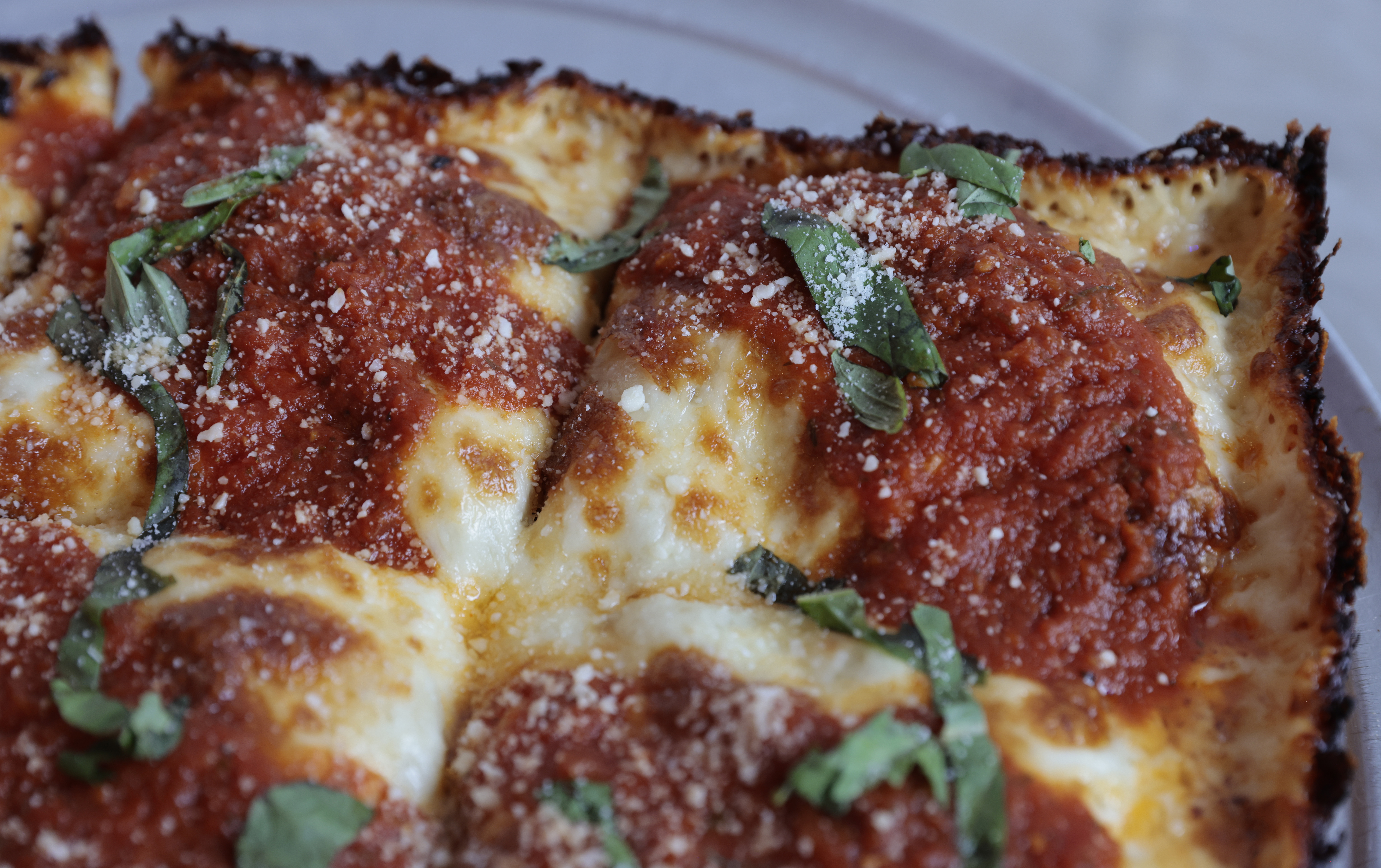 A crispy corner of a Detroit-style pizza topped with basil
