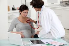 A doctor checks a pregnant woman's heart rate with a stethoscope.